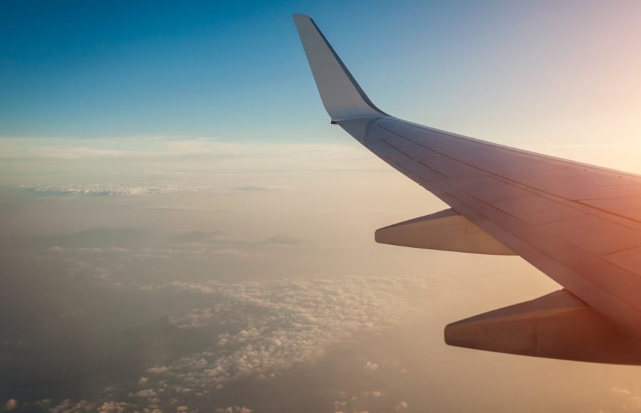 Plane window view of clouds and islands surrounded by sea and airplane wing. Traveling and vacation concept