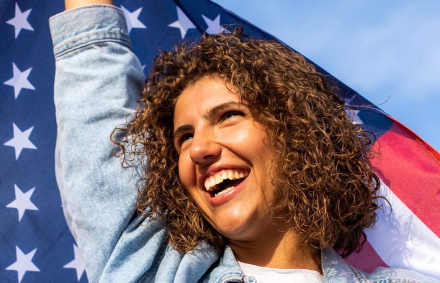 Slim beautiful woman holding USA flag celebrating Independance US day. Candid portrait of curly haired woman
